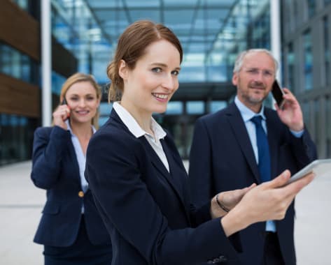 businesswoman-using-digital-tablet-while-colleagues-talking-mobile-phone