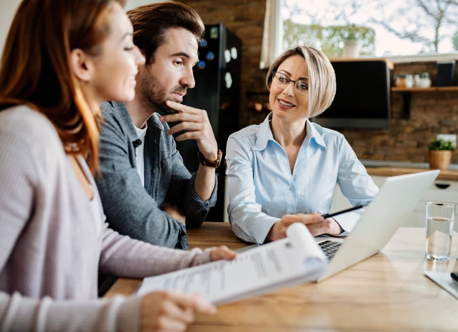 smiling-financial-advisor-using-laptop-while-having-meeting-with-young-couple